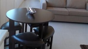 Una sala de estar con una mesa redonda y dos sillas, un sofá, y un cuadro en la pared.