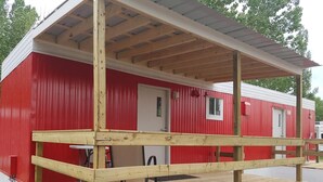 Un edificio rojo y blanco con terraza de madera y zona cubierta.