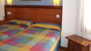 A double bed with a colorful quilt, a wooden headboard, two bedside lamps, and a painting on the wall. - Hostal Platja (Cambrils)
