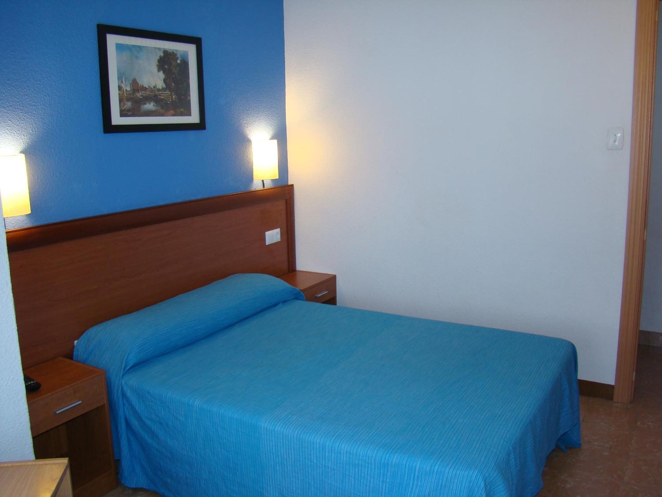 Una cama individual con cabecera de madera, una mesita de noche y un cuadro colgado en la pared.