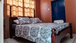 A bedroom with a bed, a blue door, and a window with curtains.