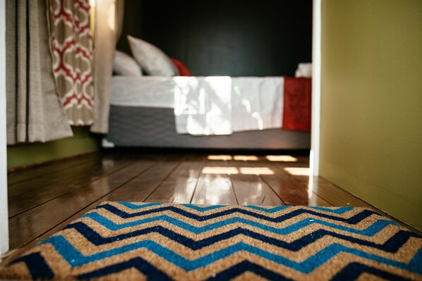 Un suelo de madera que conduce a una cama con una colcha y almohadas estampadas.