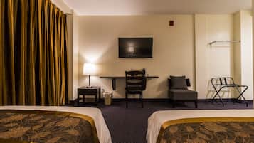 Habitación de hotel con dos camas, un escritorio con silla, televisor montado en la pared y una ventana con cortinas.