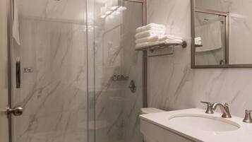 A modern bathroom with a glass-enclosed shower, a white toilet, and a sink with a mirror above it.