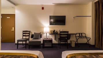 A hotel room with two beds, a desk, a chair, a lamp, and a TV on the wall.