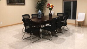 A conference room with a large table, black chairs, a vase with colorful flowers, a painting on the wall, and a potted plant.
