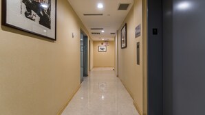 A hotel hallway with a polished floor, framed artwork on the walls, and an exit sign.