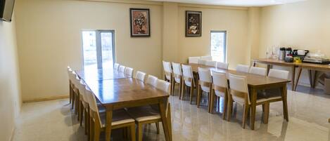 Una amplia sala de conferencias con una larga mesa de madera y sillas blancas, equipada con una estación de café.