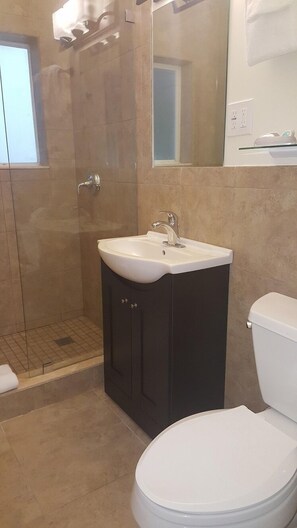 A bathroom with a white toilet, a sink with a mirror above it, and a shower area. - Le Cabanon Motel (Pompano Beach)