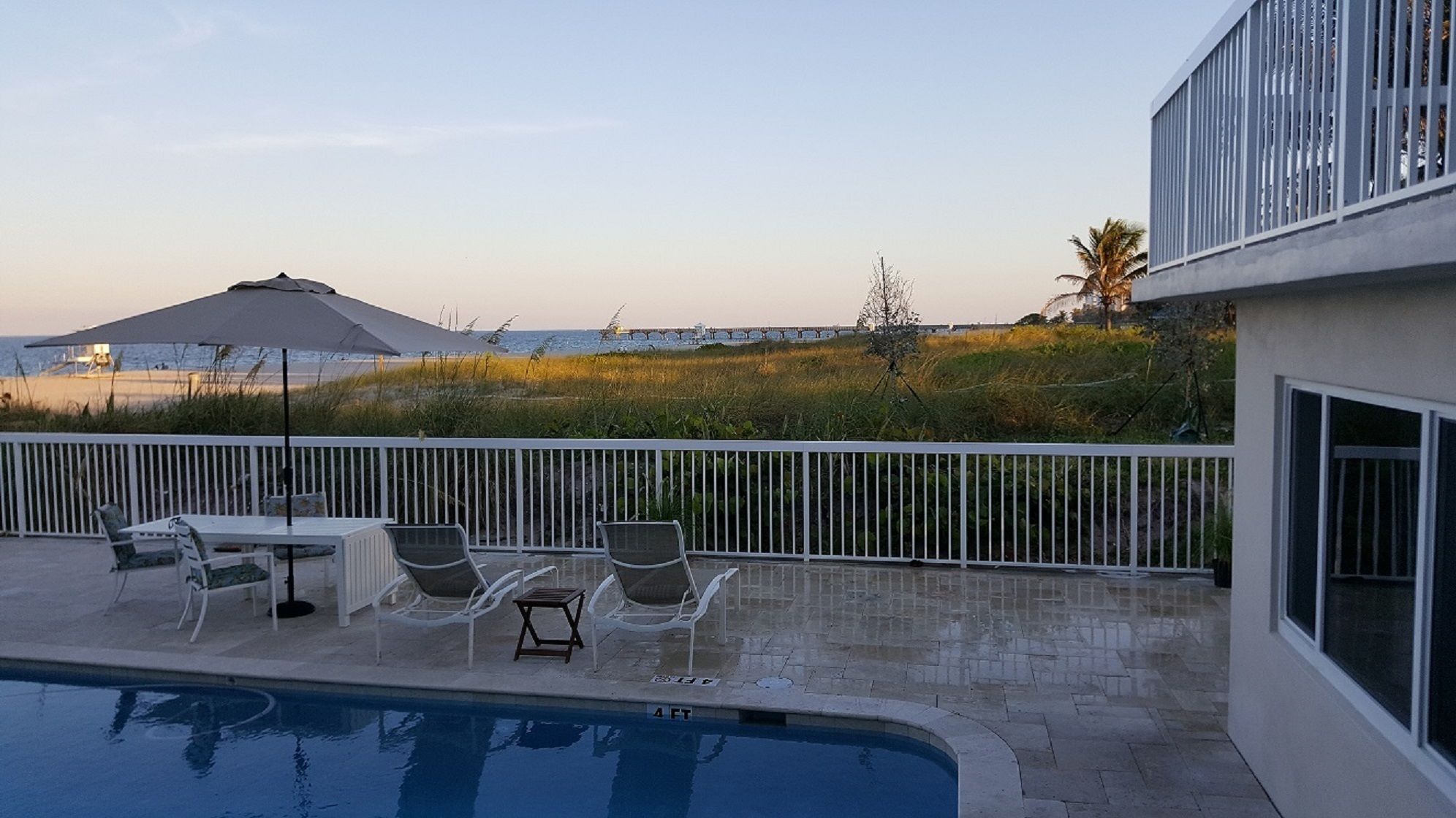 A poolside area with a view of the beach, outdoor furniture, and a building with large windows.