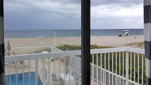 Vista da praia a partir de uma varanda, com piscina, espreguiçadeiras e posto de salva-vidas.