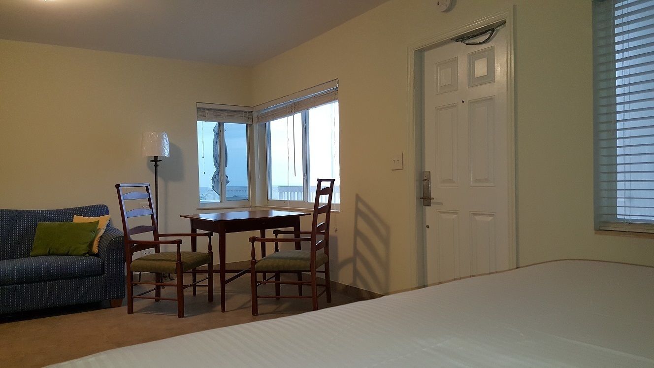 A room with a bed, a sofa, a dining table with chairs, and a window with blinds.