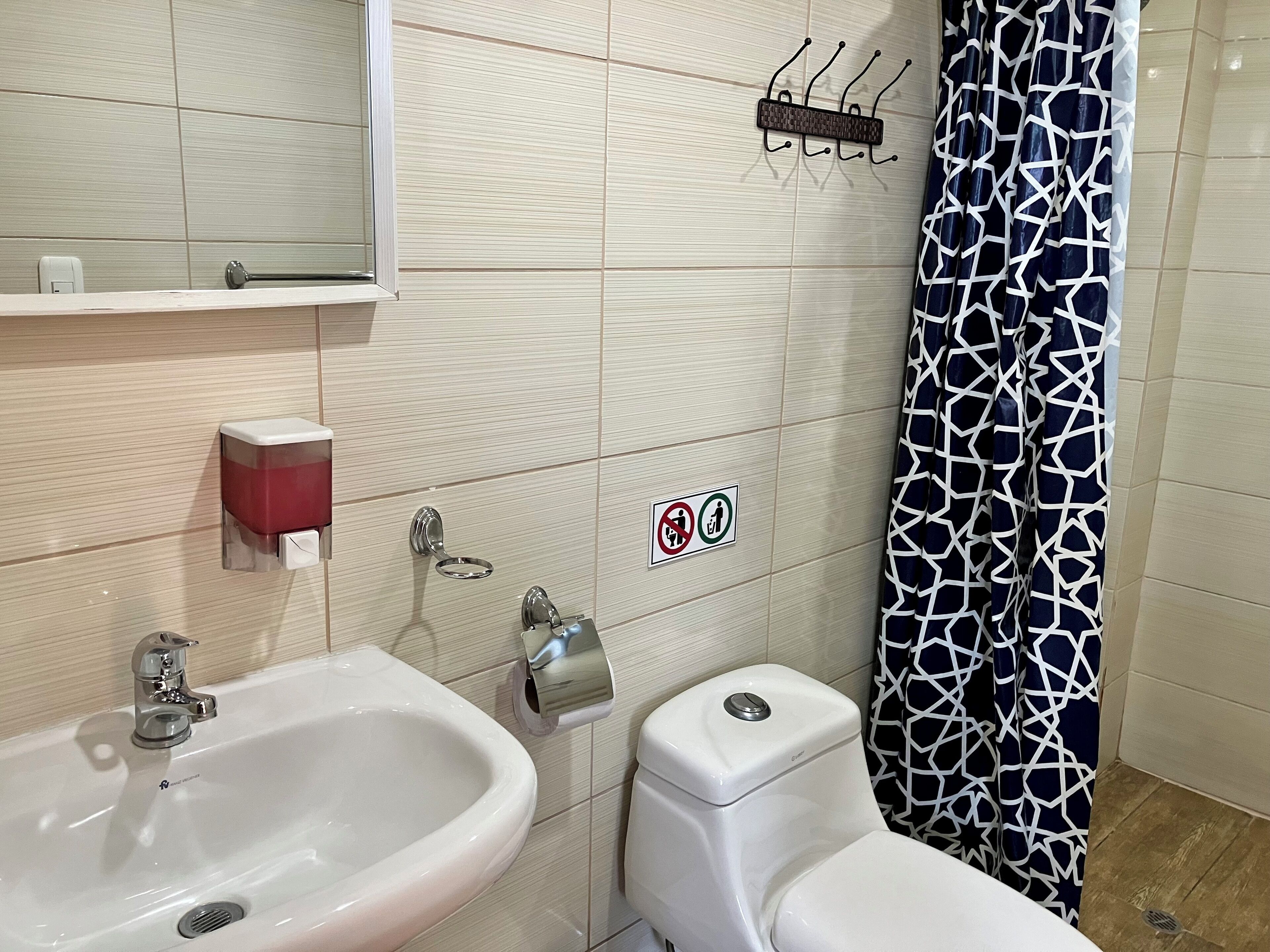 Une salle de bain équipée d’un lavabo, de toilettes et d’un miroir. On y trouve également des sèche-mains et un distributeur de savon fixés au mur.