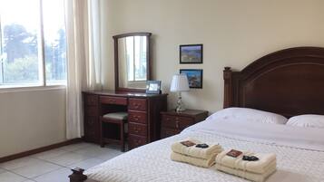 A hotel room with a bed, a wooden dresser, a mirror, a nightstand with a lamp, and two framed pictures on the wall.
