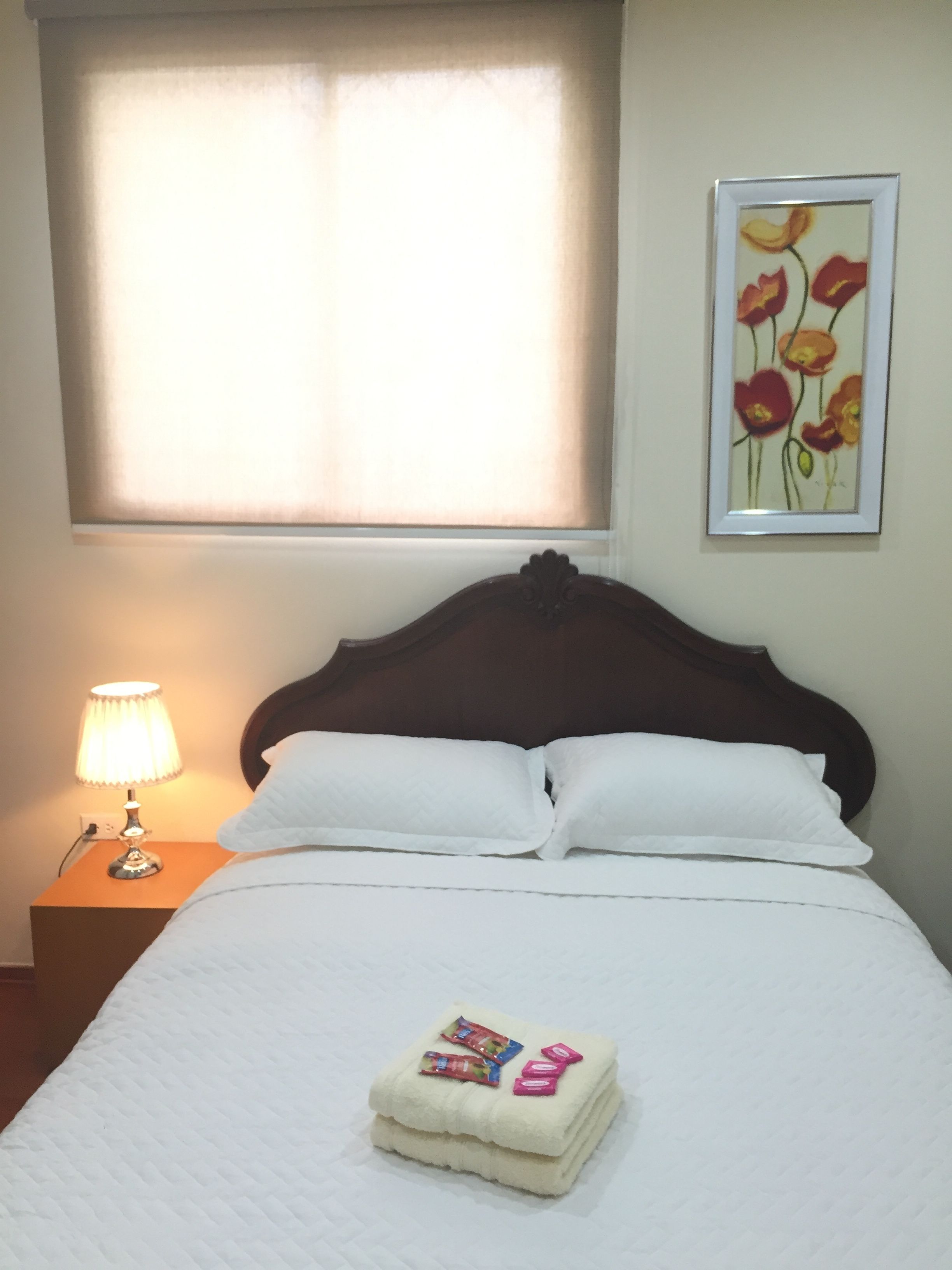 Una cama bien hecha con sábanas blancas, una lámpara de noche y una obra de arte floral enmarcada en la pared.