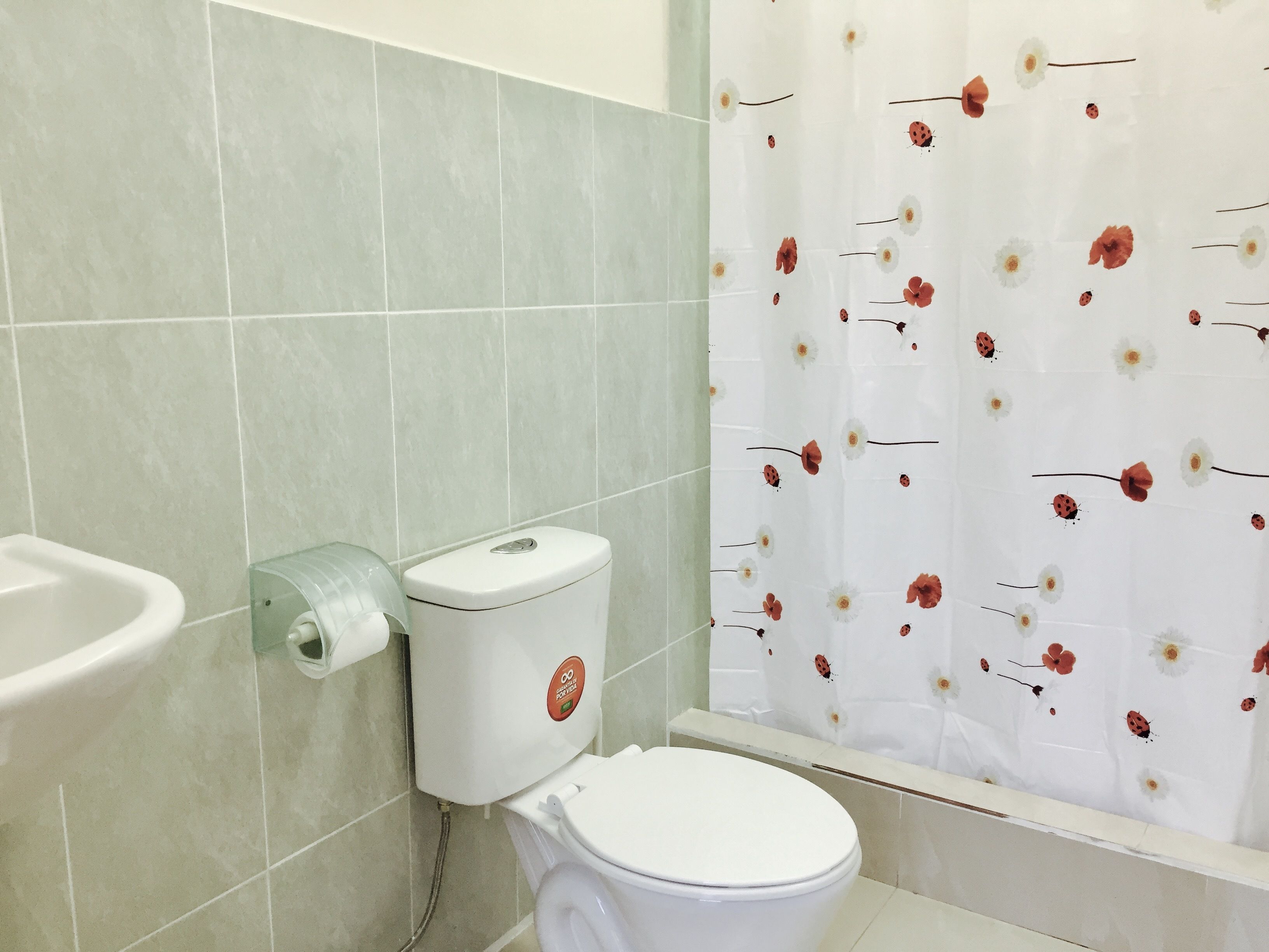 Uma casa de banho com sanita, bidé e cortina de chuveiro estampada com motivos florais.