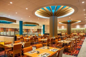 Enjoy meals prepared in the open kitchen, visible through a glass partition, amidst a spacious dining area with tables and chairs.