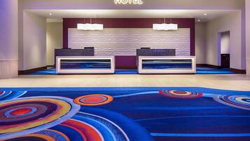 A hotel reception area with two reception desks, a wavy textured wall, and a colorful carpet.