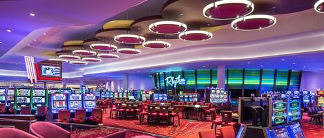 A casino with multiple gaming tables and slot machines, a prominent 'Rhythm Room' sign, and a variety of seating options.