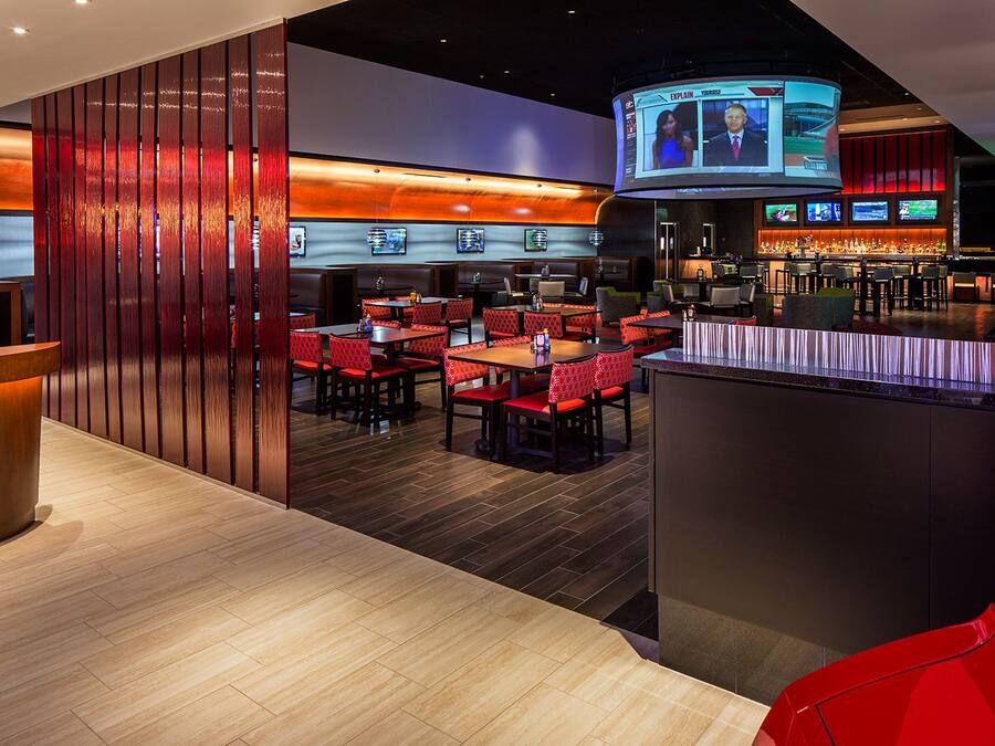 A modern restaurant with a bar area, multiple seating options, and a large screen displaying news.