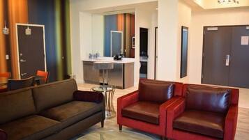 Un hall d’hôtel avec un canapé marron, un canapé rouge, une petite table ronde et un coin cuisine.