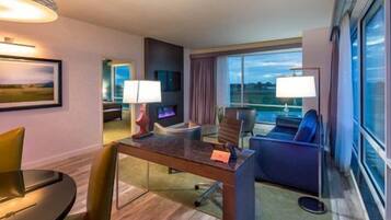 Habitación de hotel con comedor, sofá, una silla, lámpara y un gran ventanal con vistas.