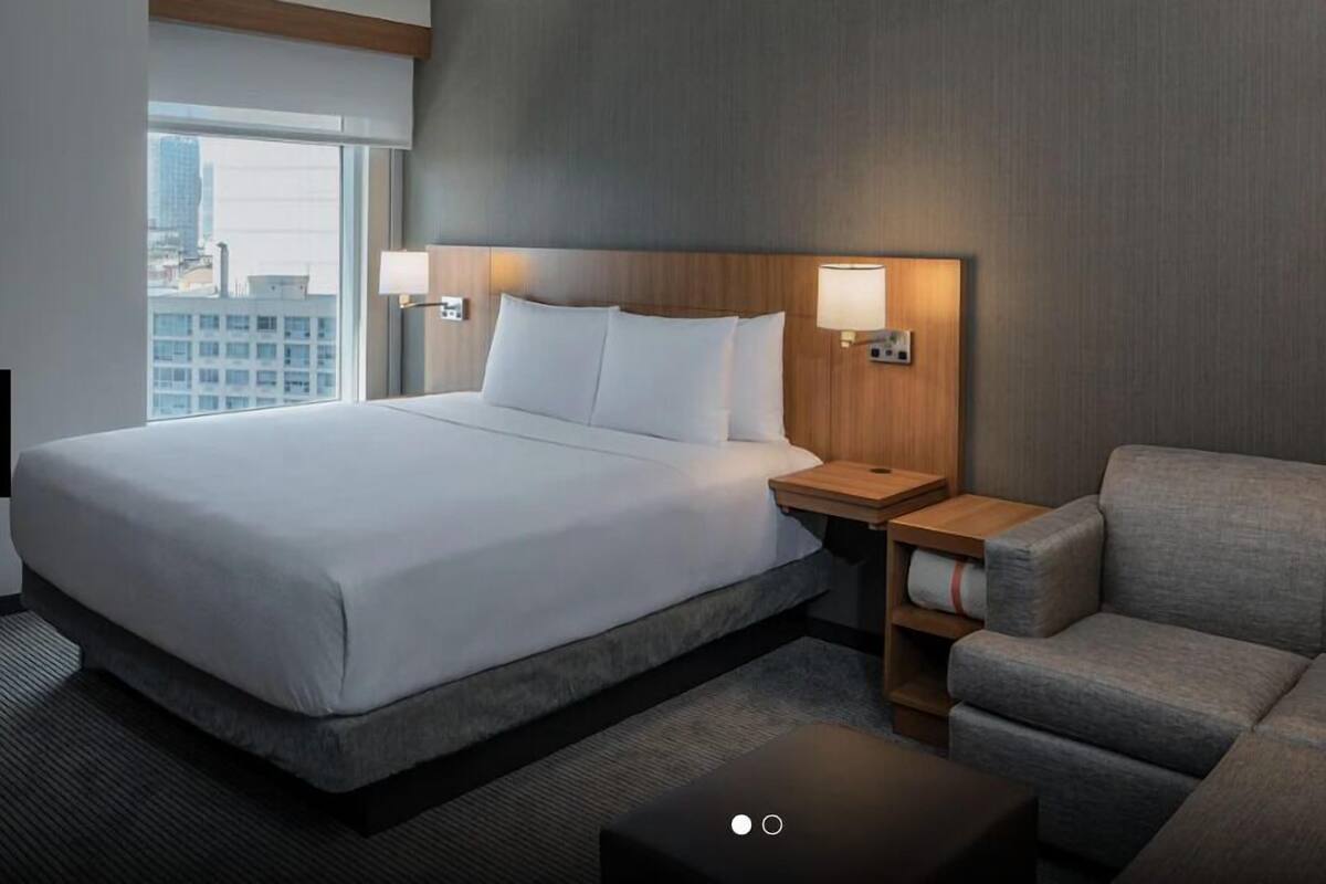 Ein Hotelzimmer mit einem großen Bett, einem grauen Sofa, einem kleinen Tisch und zwei Wandlampen.