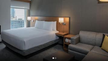 A hotel room with a large bed, a grey sofa, a small table, and two wall-mounted lamps.