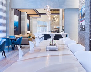 A modern hotel lobby with a long reception desk, white seating, and a large chandelier.