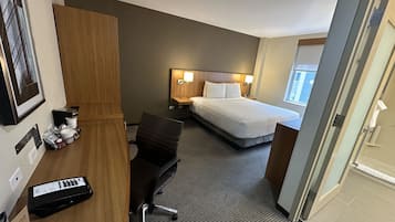 Une chambre d’hôtel comprenant un lit, une table de chevet, une lampe, une chaise, un bureau et une petite table sur laquelle se trouvent divers objets.