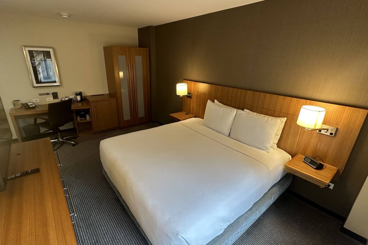Ein Hotelzimmer mit einem großen Bett, einem Schreibtisch, einem Stuhl, einem Kleiderschrank und einem Nachttisch mit Lampe.