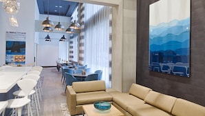 Un moderno vestíbulo de hotel con un amplio sofá beige modular, un comedor con sillas blancas y un gran cuadro abstracto en la pared.