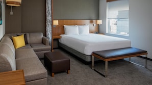 Una habitación de hotel moderna con una cama grande, un sofá, un banco y una ventana con vistas a la ciudad.