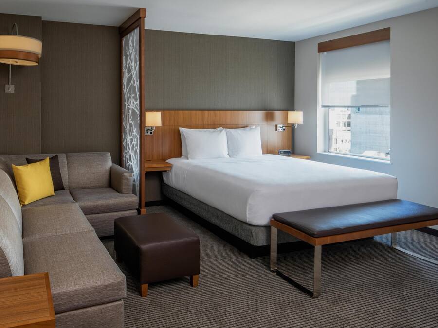 Une chambre d’hôtel moderne dotée d’un grand lit, d’un canapé, d’une banquette et d’une fenêtre donnant sur la ville.