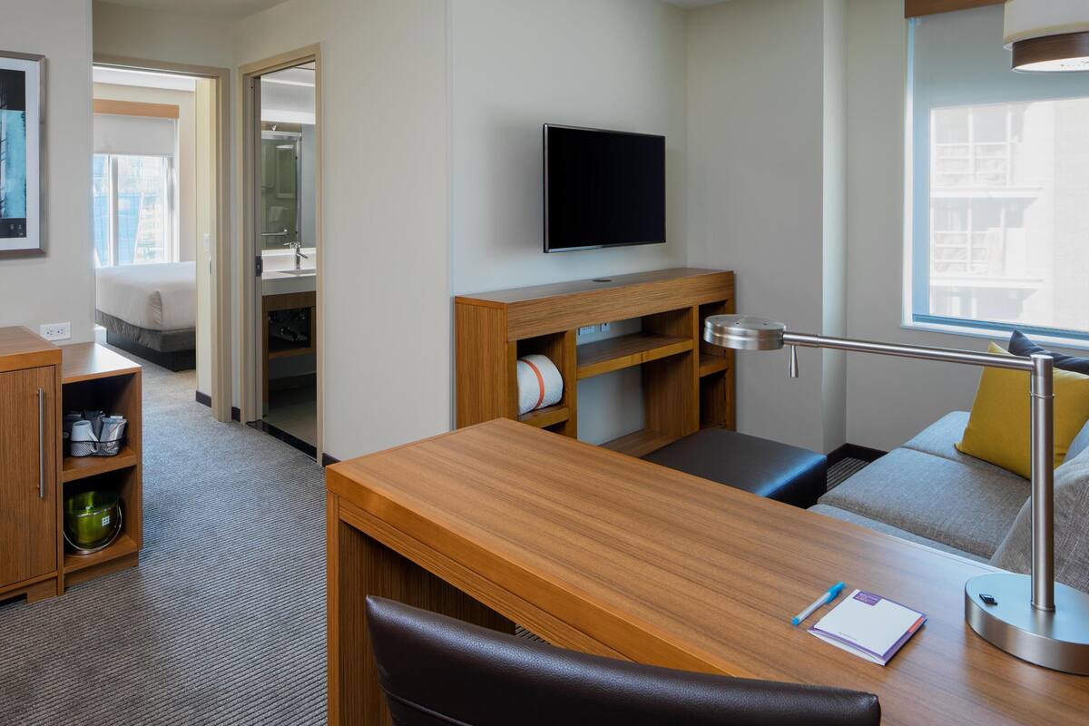 Ein Hotelzimmer mit einem Holztisch, einem Fernseher, einem Sofa und einem Fenster mit Blick.