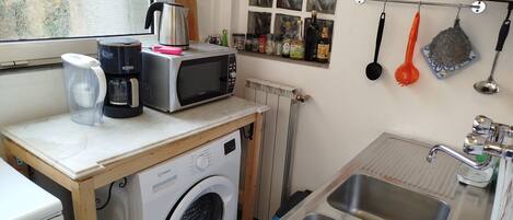 A compact kitchen with a washing machine, a microwave, a coffee maker, and a sink.