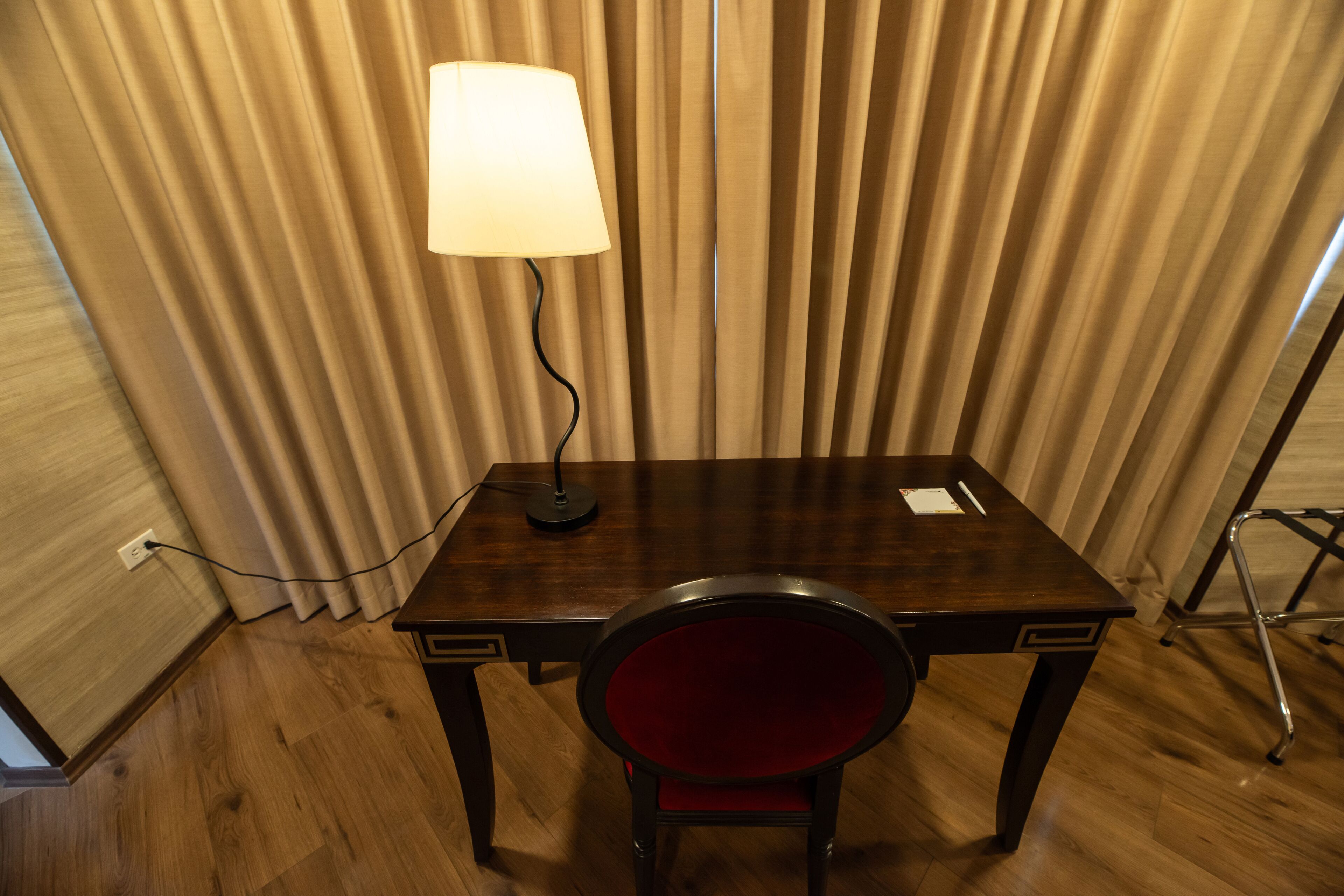 A wooden desk with a lamp, a red chair, and a curtain backdrop.