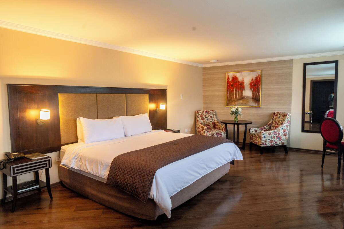 A hotel room with a large bed, bedside tables, a desk, a chair, and a small table with a vase.