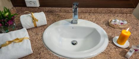 A bathroom sink with a mirror above it, a towel with a yellow ribbon, a candle, and toiletries on the countertop.