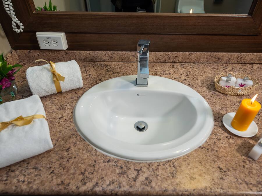 A bathroom sink with a mirror above it, a towel with a yellow ribbon, a candle, and toiletries on the countertop.