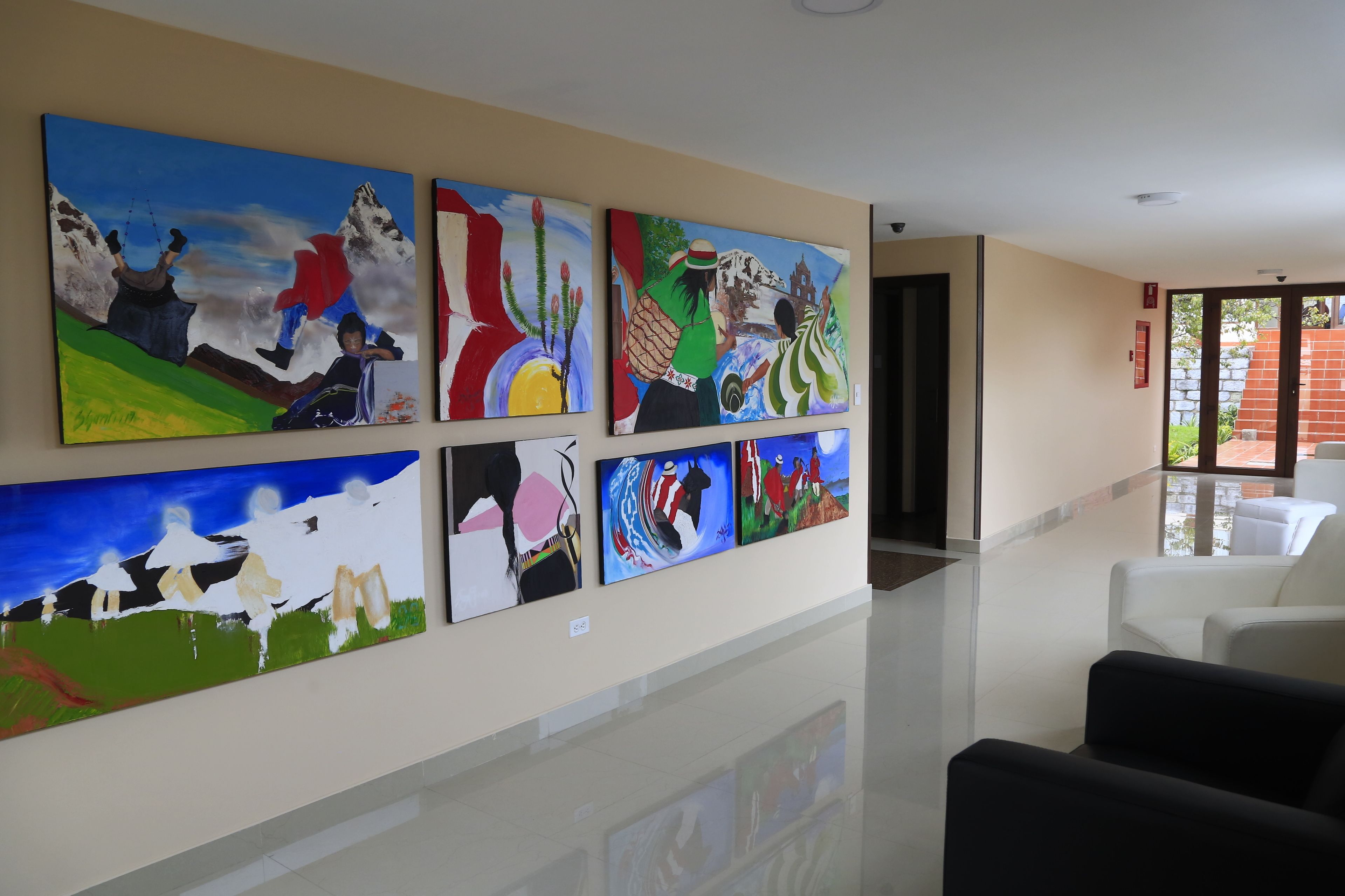 Un vestíbulo de hotel con varias pinturas en la pared, piso pulido y una zona de estar con sillas blancas.