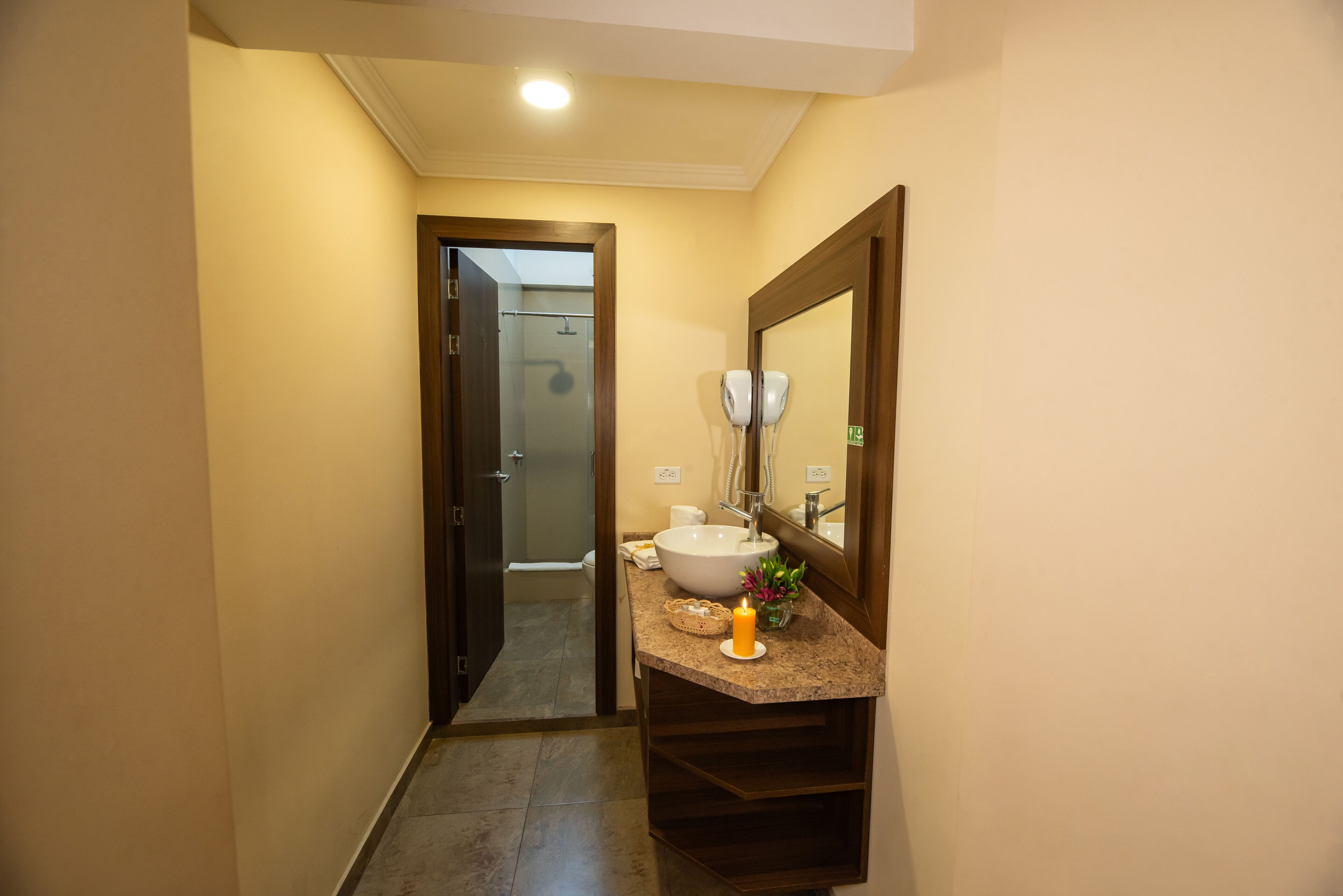 Un pasillo estrecho que conduce a un baño con lavamanos, espejo y una vela encendida.