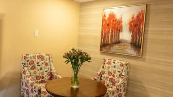 Una habitación con dos sillas de estampado floral, una mesa de madera y un cuadro de árboles otoñales en la pared.