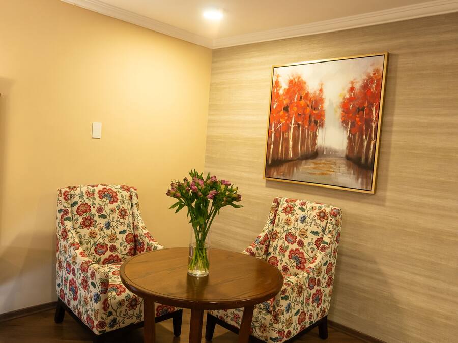 Una habitación con dos sillas de estampado floral, una mesa de madera y un cuadro de árboles otoñales en la pared.