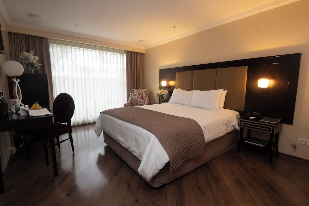 A hotel room with a large bed, a desk with a chair, a nightstand, and a lamp.