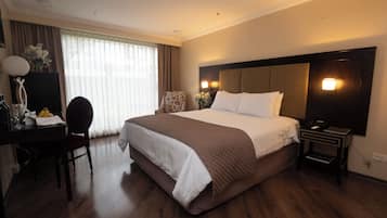 Habitación de hotel con una cama grande, un escritorio con silla, una mesita de noche y una lámpara.