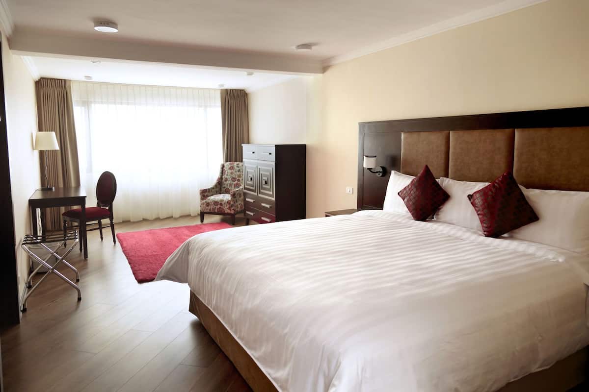 A hotel room with a large bed, a desk, a chair, a dresser, and a window with curtains.