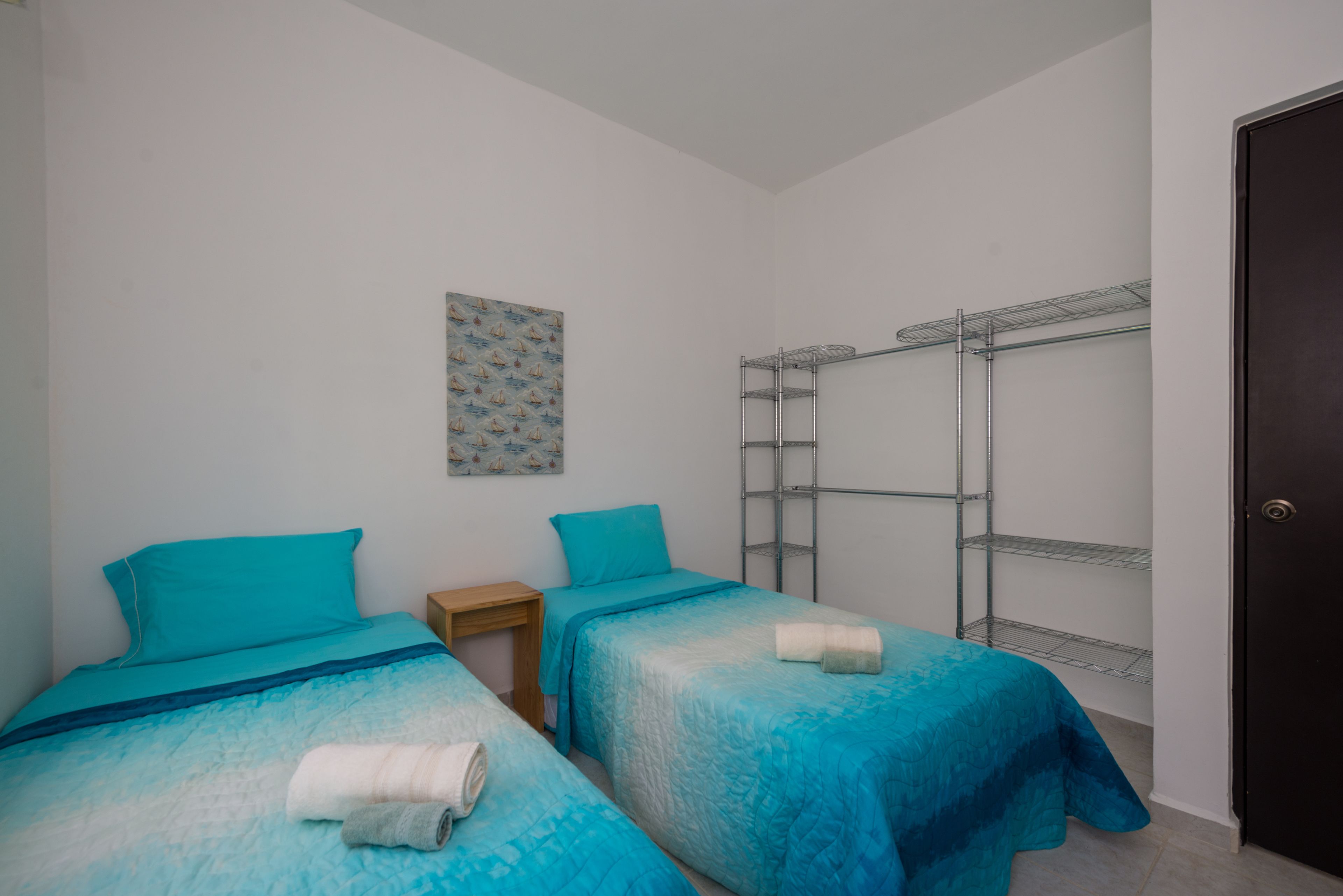 Une chambre avec deux lits, une table de chevet en bois, une étagère en métal et une porte.
