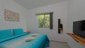Ein Schlafzimmer mit Bett, Fernseher, Fenster und einem Bild an der Wand.