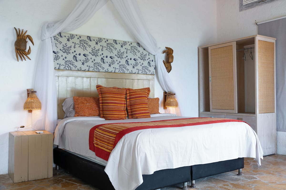 Un dormitorio con cama, lámparas de noche, mesita de noche, armario y un cabecero decorativo.